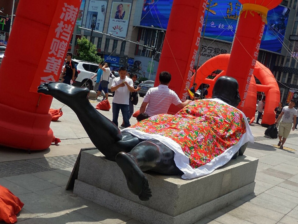 A naked female statue is covered by a quilt with a traditional Chinese design.