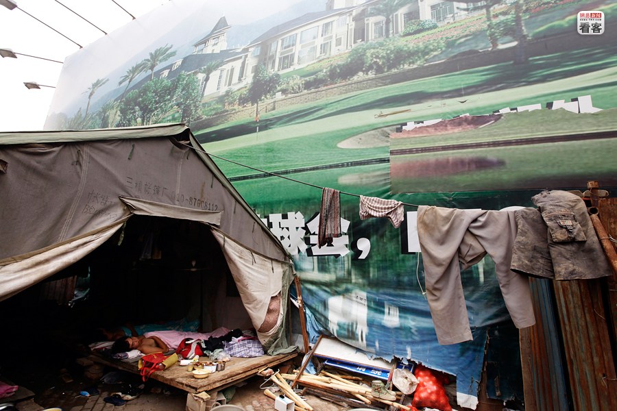 several construction workers are sleeping in a tent under a huge real estate advertising board in Beijing 